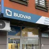 Logo firmy BUDVAR z napisem "OKNA DRZWI ROLETY" na fasadzie budynku.
