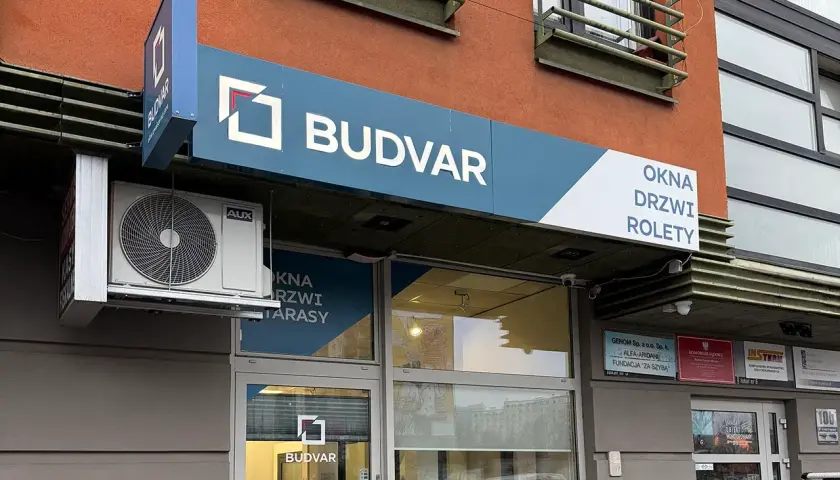 Logo firmy BUDVAR z napisem "OKNA DRZWI ROLETY" na fasadzie budynku.
